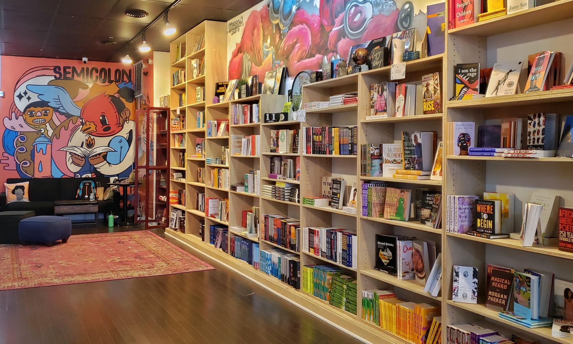 The inside of a bookstore, with the wall to the right covered in books and the far back wall featuring artwork.